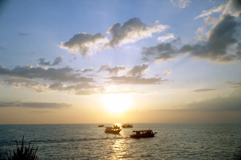 Small boats drift on calm waters as the sun sets over the sea in Cambodia.