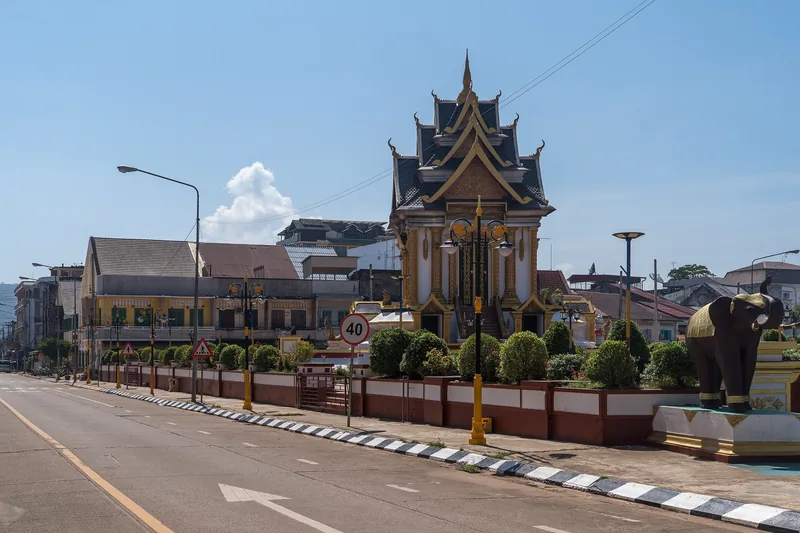 A pyramid-roofed shrine and elephant statue stand along a quiet street in Pakse, Laos.