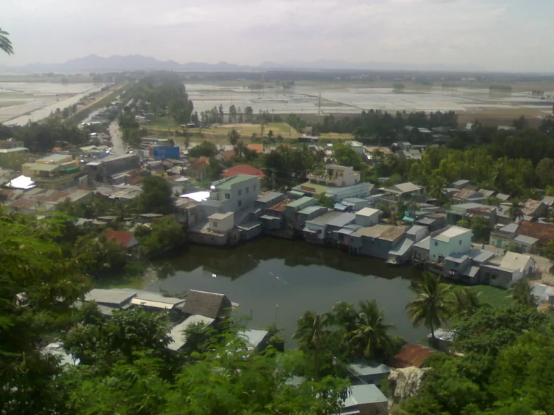 Elevated view from Nui Sam hill overlooking Chau Doc town with rooftops, a pond, and rice fields beyond.