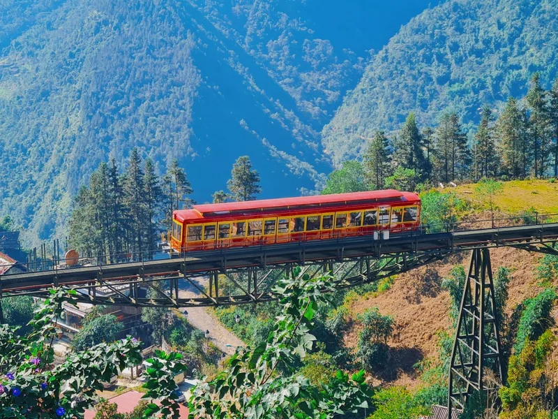 A red funicular train crosses an elevated bridge amid green mountains on Fansipan in Sapa.