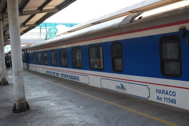 A blue Vietnam Railways carriage stands at a covered platform in Hanoi station.