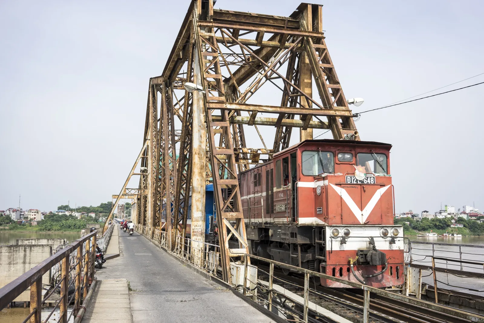 A red locomotive crosses the steel trusses of Long Bien Bridge in Hanoi.