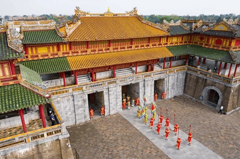 Costumed guards parade in the courtyard of Hue's Imperial Citadel beneath ornate yellow and green tiled rooftops.