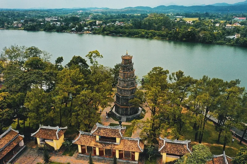 Aerial view of Thien Mu Pagoda's tower rising above pine trees beside the Perfume River in Hue.