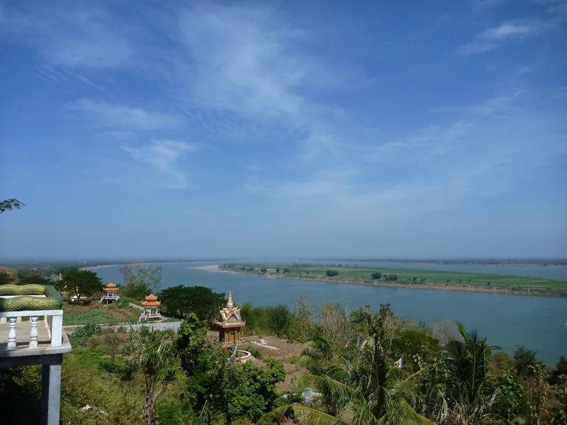 Wide view of the Mekong River from Han Chey temple hill near Kampong Cham, with small pagoda pavilions amid greenery.