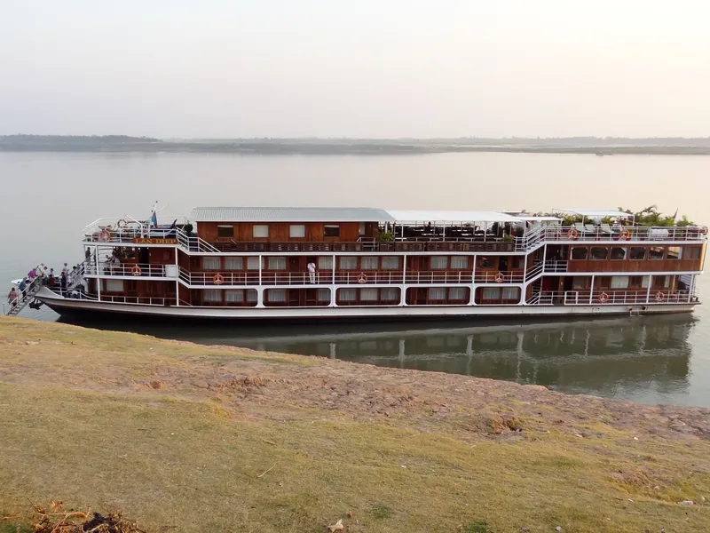 A multi-deck river cruise ship docks along the Mekong riverbank near Kampong Cham at dusk.