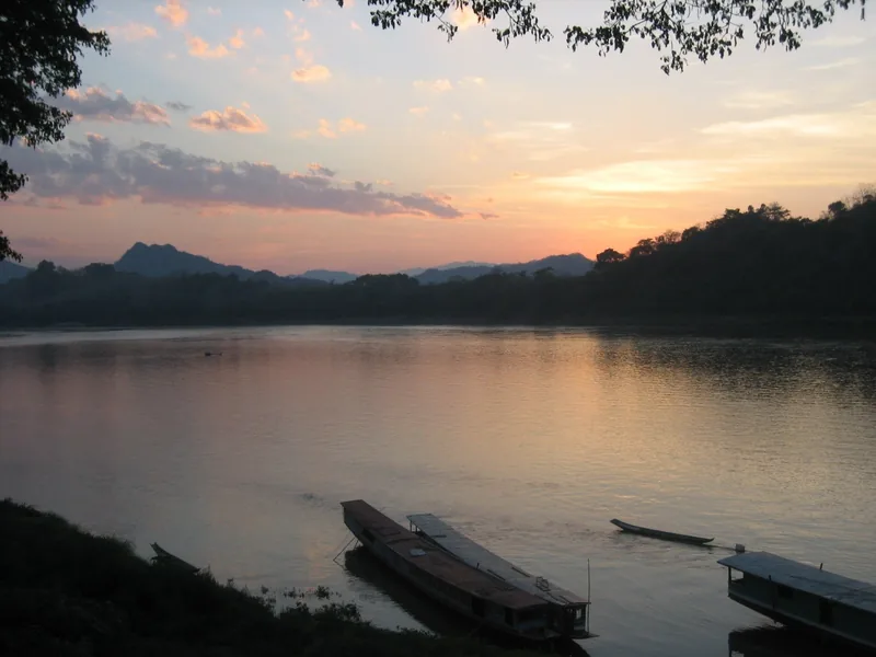 Sunset glow over the Mekong River with wooden boats moored near the bank in Luang Prabang, Laos.