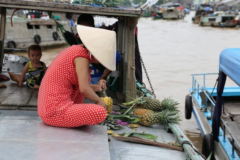 A woman in a conical hat peels pineapples on a boat at the Cai Rang floating market in Can Tho.