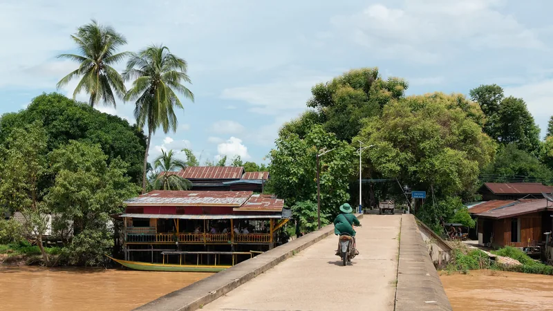 A motorbike rider crosses a concrete bridge linking Don Det and Don Khon in Si Phan Don, Laos, over a muddy river.