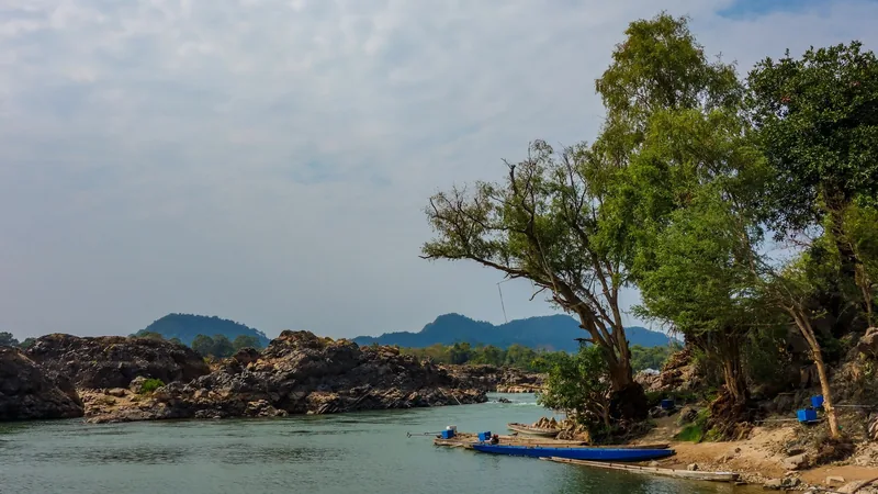Rocky river islets and a wooden boat along the Mekong at Si Phan Don, Laos