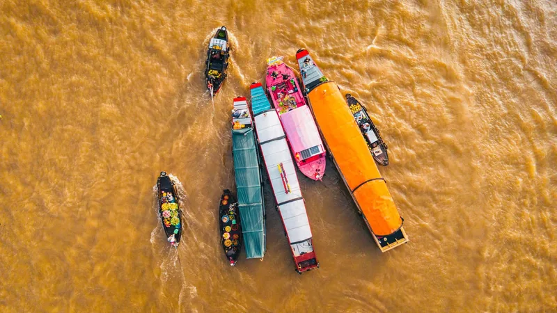 Aerial view of colorful boats gathered on muddy river water in a floating market setting.