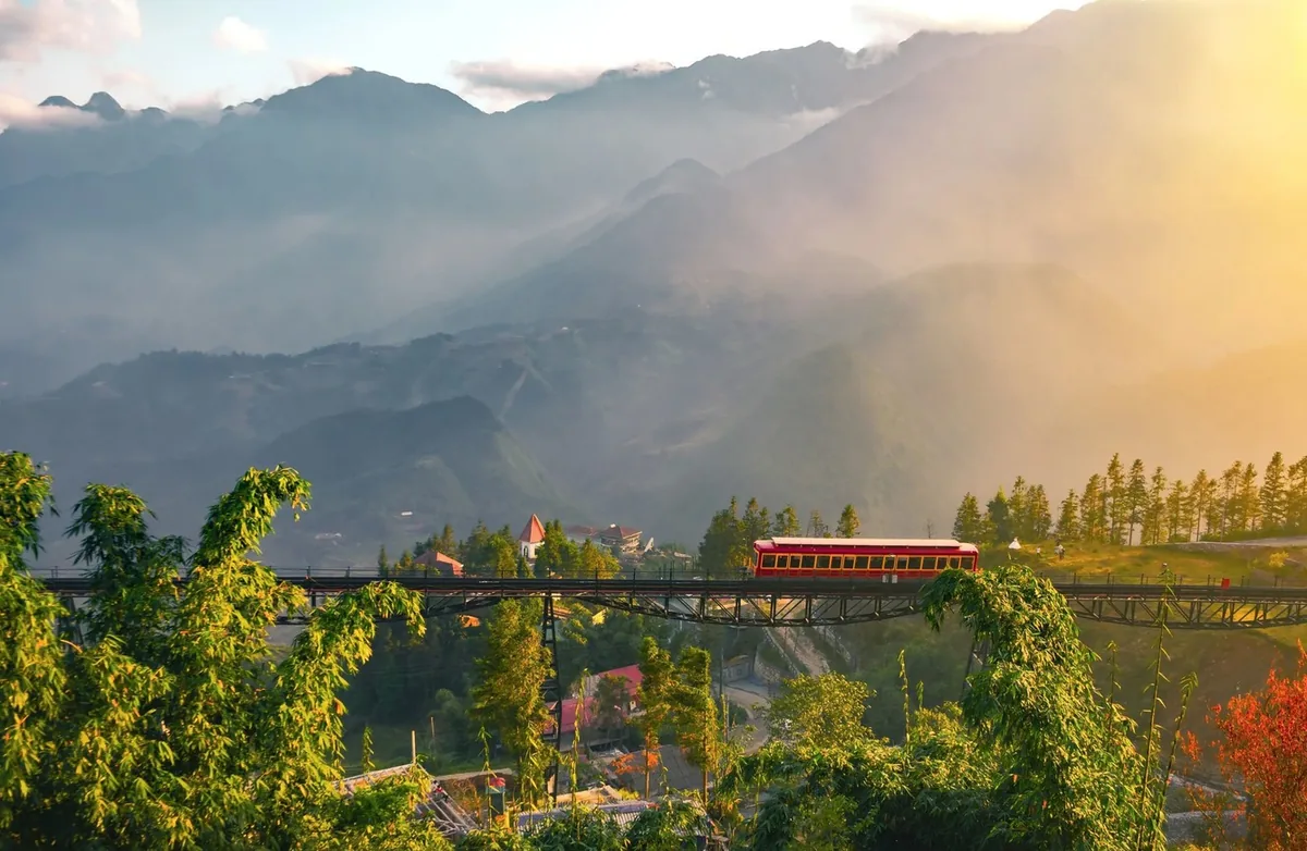 A red funicular train crosses a high bridge above misty mountains near Fansipan in Sapa.