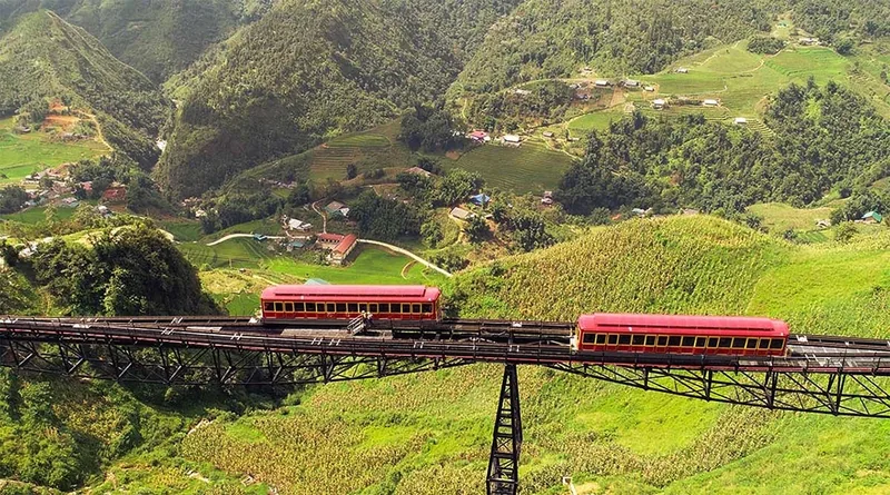 A red funicular train crosses a high trestle bridge over the green Muong Hoa valley near Fansipan.