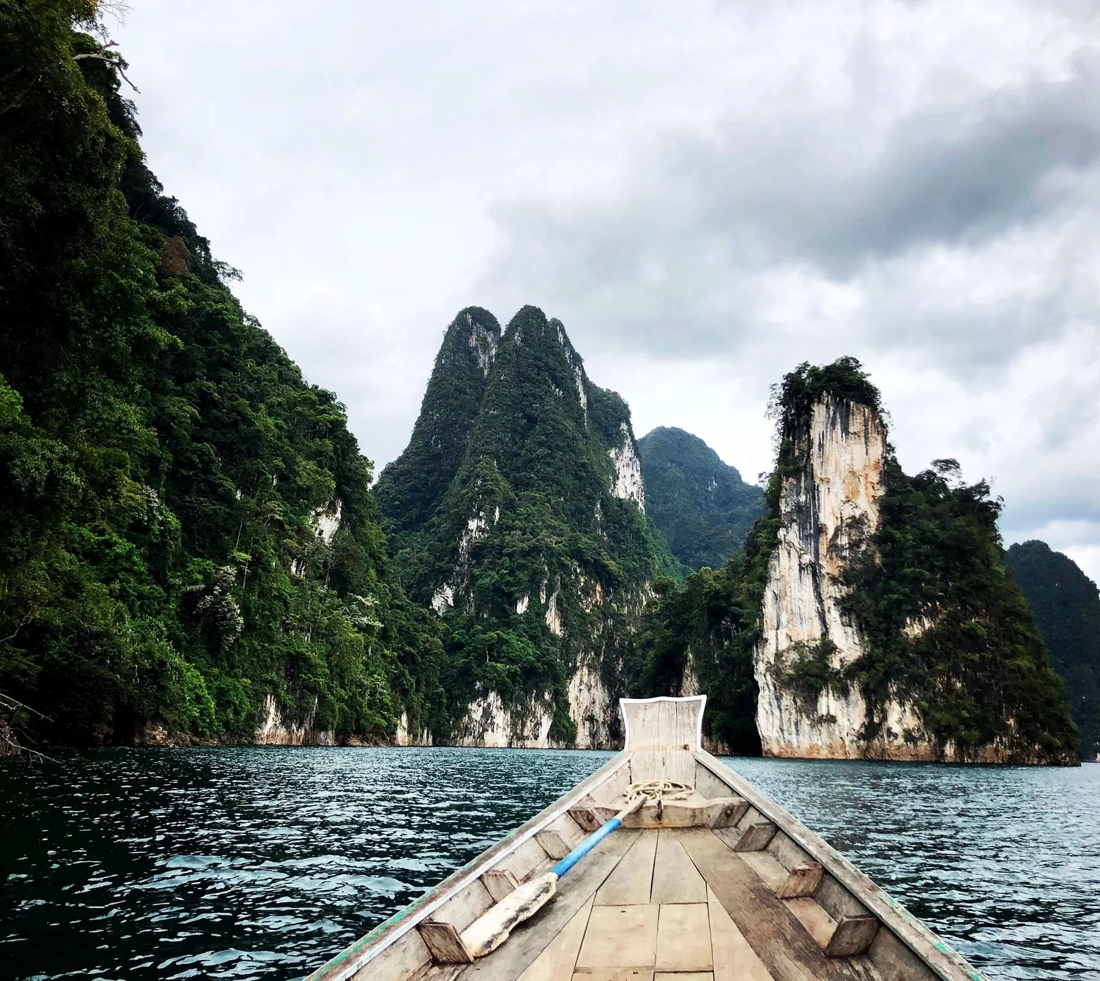 A longtail boat glides across a lake toward towering limestone karsts covered in dense jungle.