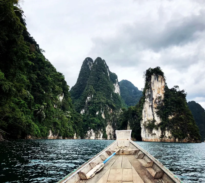 A longtail boat glides across a lake toward towering limestone karsts covered in dense jungle.