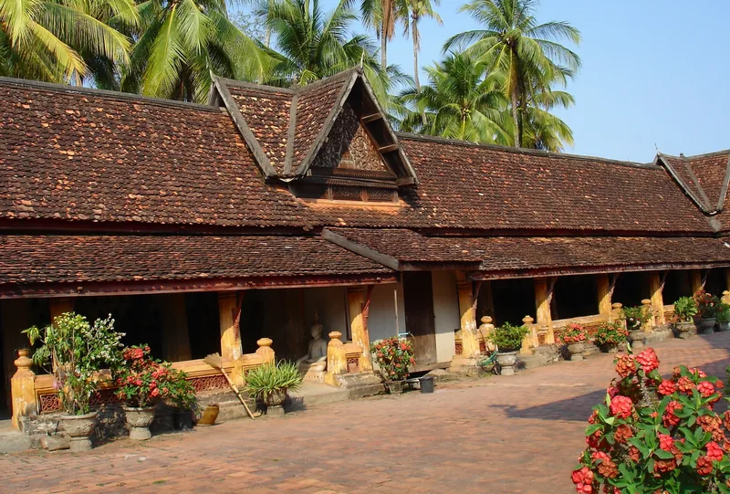 A tiled, low-sloped roof and open pavilion line the courtyard of Wat Si Saket temple in Vientiane, framed by potted flowers.